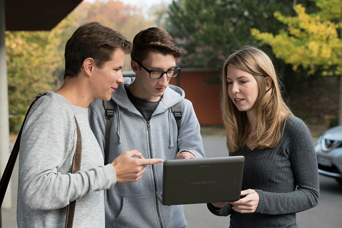 Drei Studierende schauen gemeinsam auf einen Laptop und diskutieren darüber. 