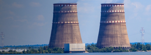Im Bild sind die zwei Kühltürme des Kernkraftwerks Saporischschja zu sehen. Davor befindet sich ein Gewässer.