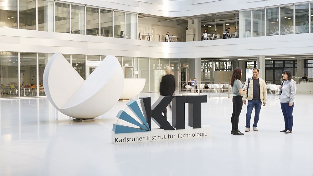 Foyer des Mathegebäudes am Campus Süd mit Skulptur und Studierenden und Forschenden im Gespräch.