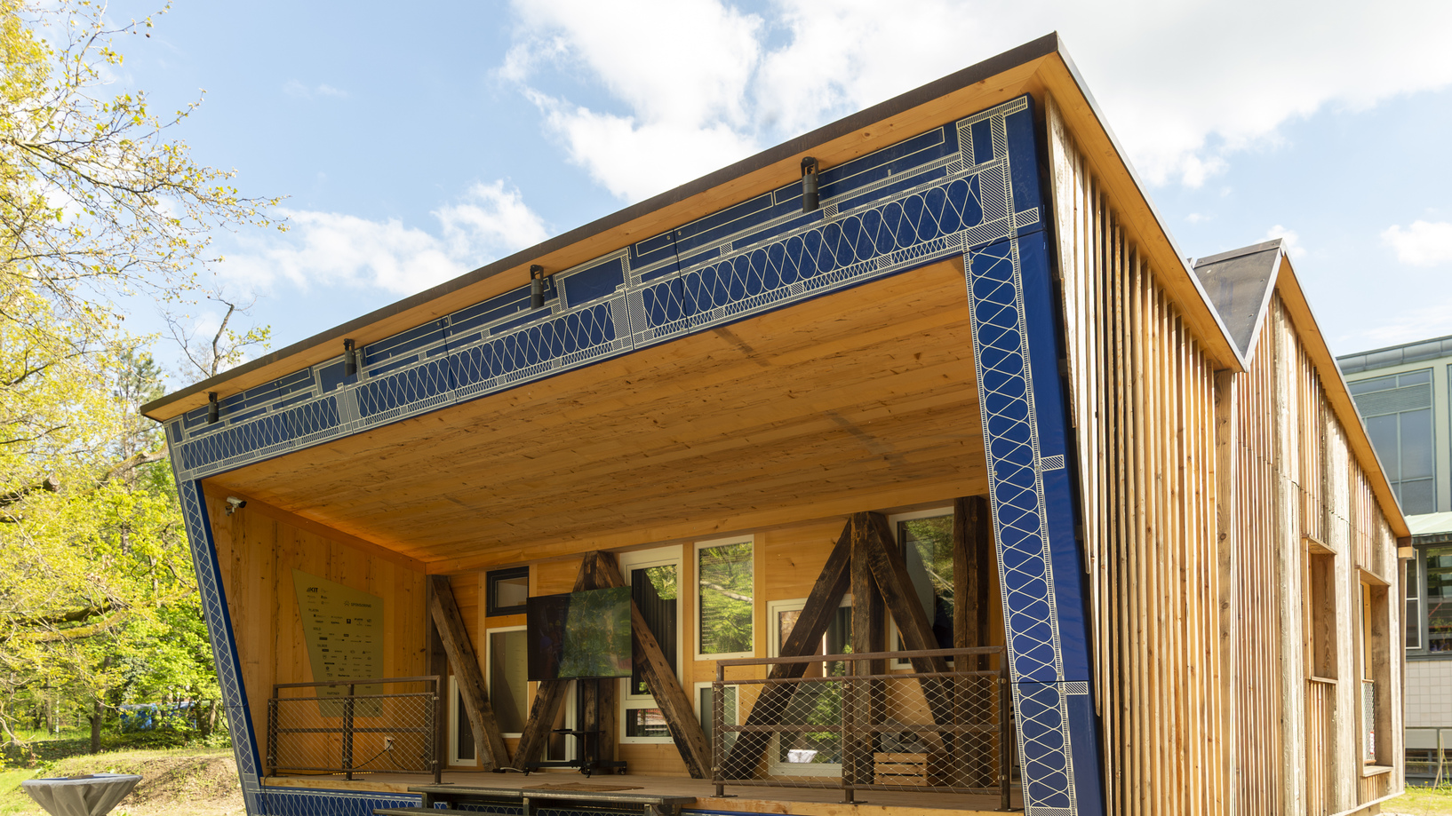 KIT Modern wooden building with blue accents and large windows under a sunny sky.