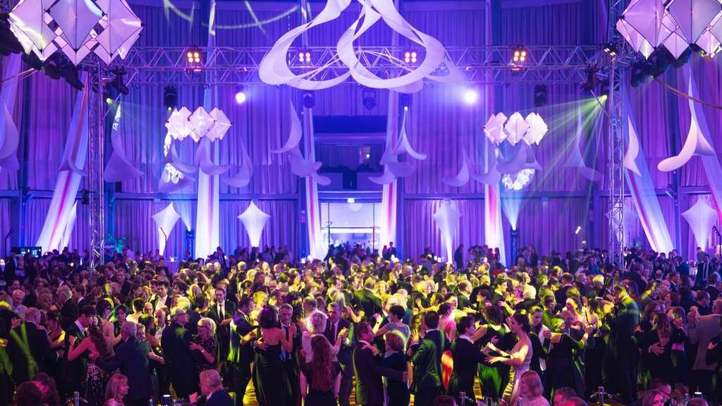 Große Tanzveranstaltung mit elegant gekleideten Gästen in festlich beleuchtetem Saal.