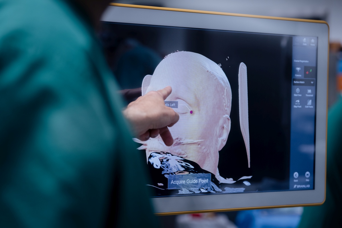 Chirurg zeigt auf eine 3D-Rekonstruktion eines menschlichen Schädels auf einem medizinischen Monitor.