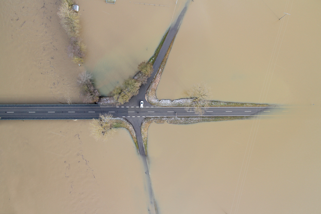 aerial view of a car standing on a crossroad where all roads leading away are flooded