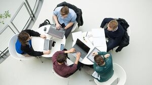 Symbolbild: Fünf Studierende sitzen um zwei Tische und arbeiten an Notebooks und Tablets