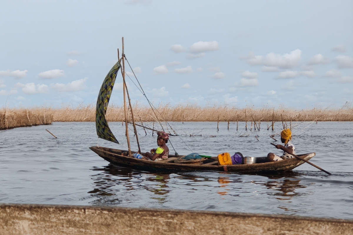 Zwei Personen fahren mit einem Holzboot über eine überflutete landwirtschaftliche Fläche.
