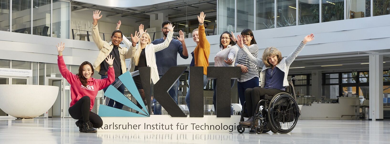 Several people standing behind a big KIT logo, a person is sitting in a wheelchair