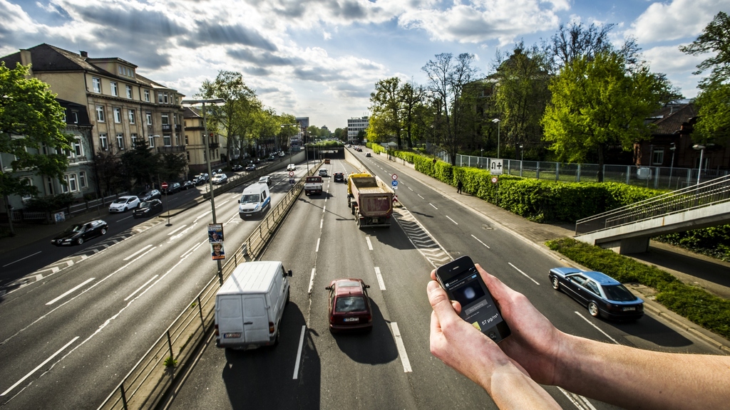 Hand mit Smartphone auf einer Brücke unter der Autoverkehr hindurchströmt