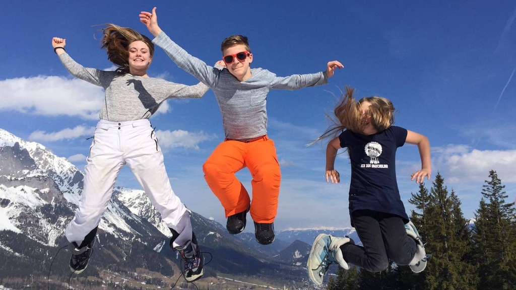 Drei springende Kinder in Winterbekleidung vor Bergen