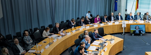 Sitzungssaal, in dem zahlreiche Menschen sitzen und konzentriert zum Rednerpult schauen.