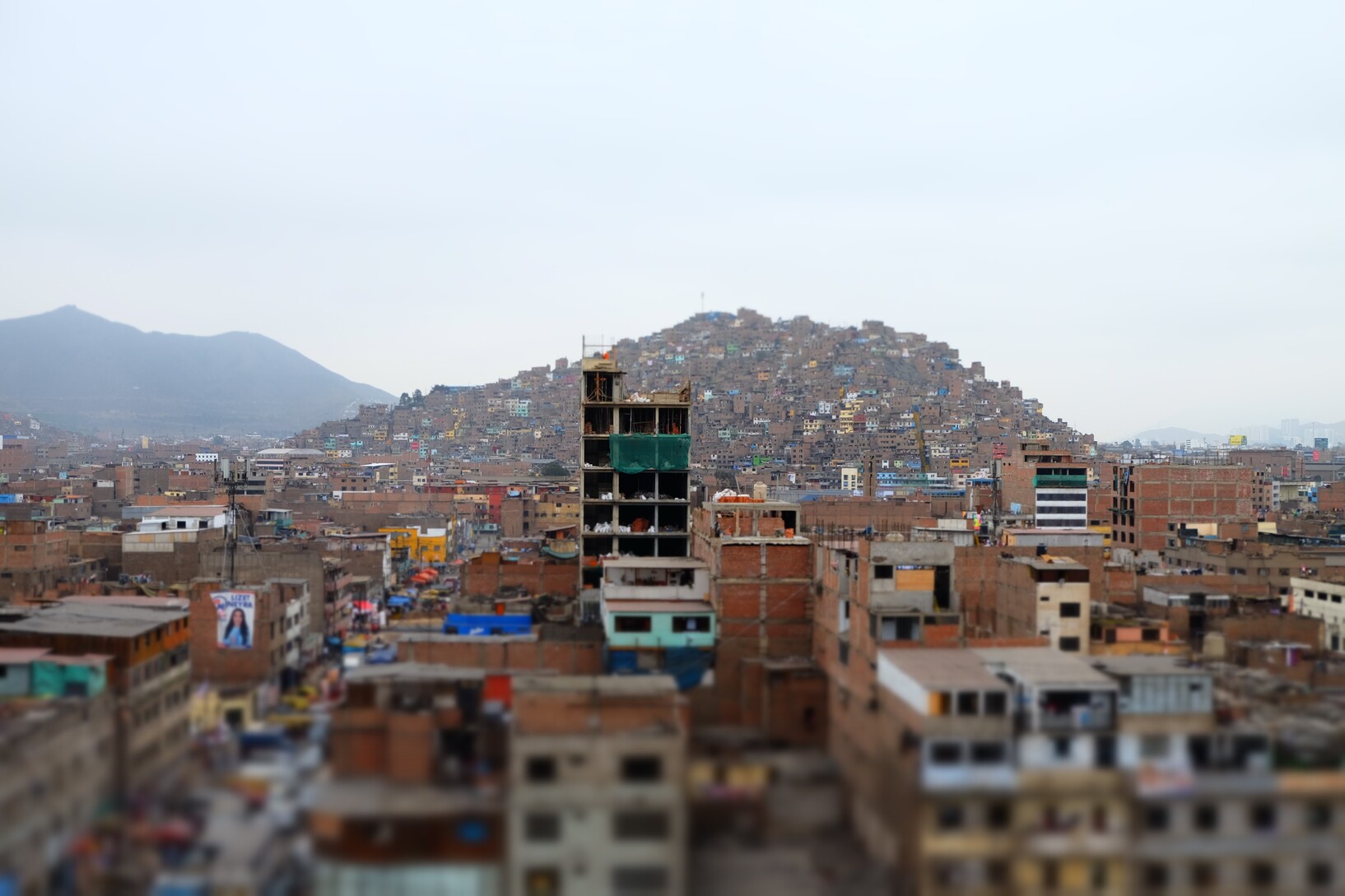 The image is focused on an unfinished high-rise building. A densely built-up hill can be seen in the background. 