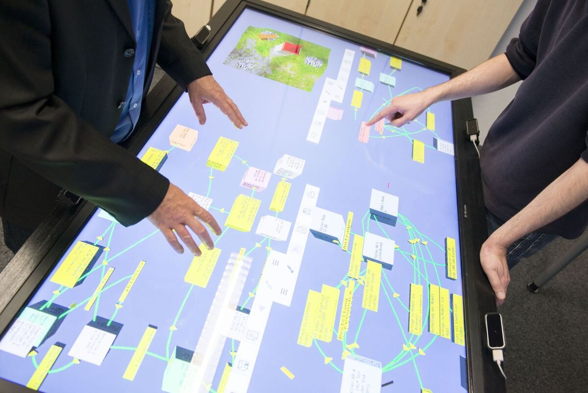 Zwei Menschen arbeiten an einem Touchscreen Tisch, die Hände berühren das Display