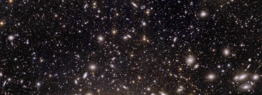 Aufnahme des Galaxienclusters Perseus mit rund Eintausend Galaxien im Vordergrund und mehr als Einhunderttausend im Hintergrund. Die Galaxien sind als kleinere und größere Lichtpunkte erkennbar. Einzelne auch als Spiralen.