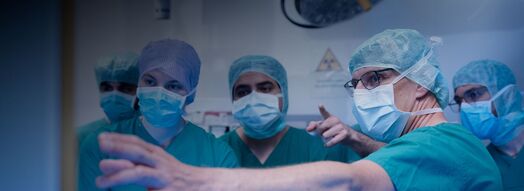 Medical team and KIT students in scrubs and masks examining a screen in a operating room.