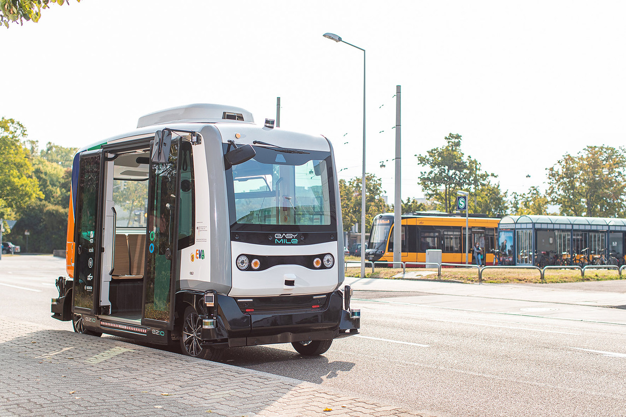  an autonomous shuttle in front of a yellow city-train