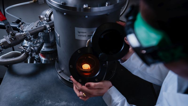 Chiara Bellamoli, KIT Development of high-temperature composite materials: Scientist in lab gear observing a glowing sample inside a vacuum chamber.
