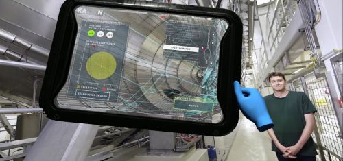 Einblick in die VR-Anwendung: Der Physiker Dr. Manuel Klein erklärt neben dem Hauptspektrometer-Tank das KATRIN-Experiment. Mit dem virtuellen Tablet können die Benutzer und Benutzerinnen der VR-Anwendung das Experiment steuern. (Quelle: Screenshot aus der Anwendung)