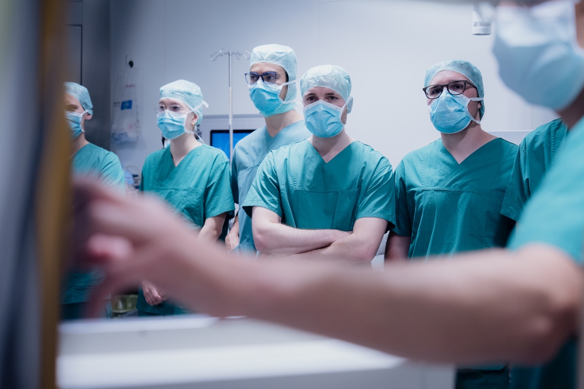Eine Gruppe von Studierenden in grüner OP-Kleidung verfolgt die Operation.